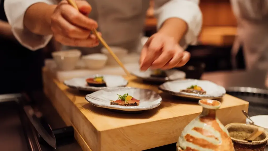 A professional kitchen pass at night, stainless steel gleaming under warm overhead light, plated dishes lined up, chefs in.