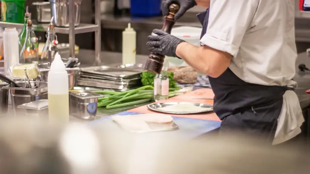 A lone chef's whites hanging on a hook in an empty, dimly lit kitchen corridor, natural light from a distant window, muted.