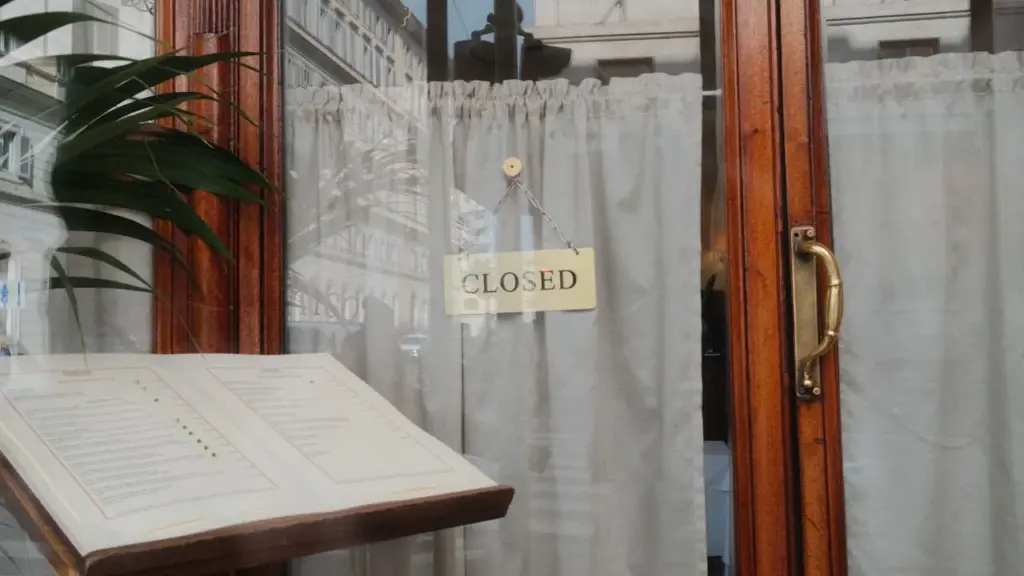 Empty British restaurant interior at dusk, closed sign on door, dim warm light over vacant tables with white linen.
