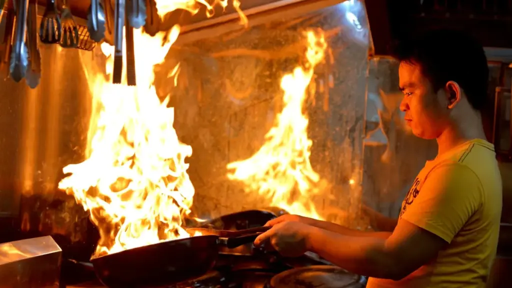 A lone chef in whites stands at the pass of an empty restaurant kitchen, back turned, gazing into a dim dining room.