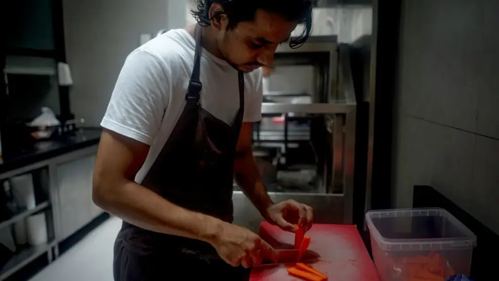 A lone young chef in whites standing in a dim commercial kitchen after service, mop bucket nearby, overhead strip lighting.